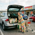 Woman putting reusable grocery bags into car trunk outside supermarket